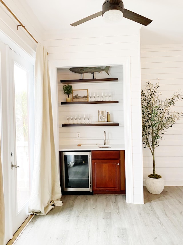 bar featuring sink, ceiling fan, wooden walls, wine cooler, and light wood-type flooring