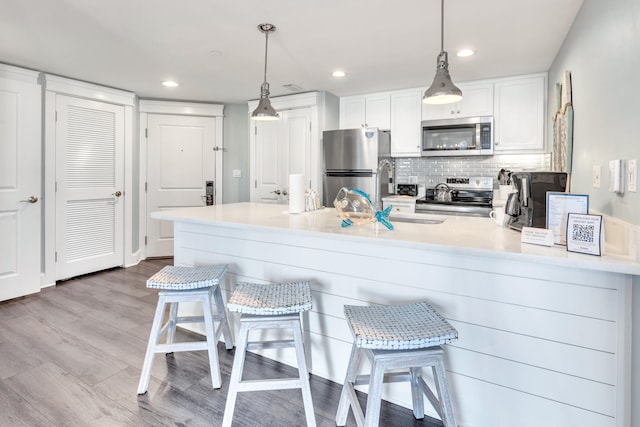 kitchen featuring appliances with stainless steel finishes, pendant lighting, sink, white cabinets, and a kitchen bar