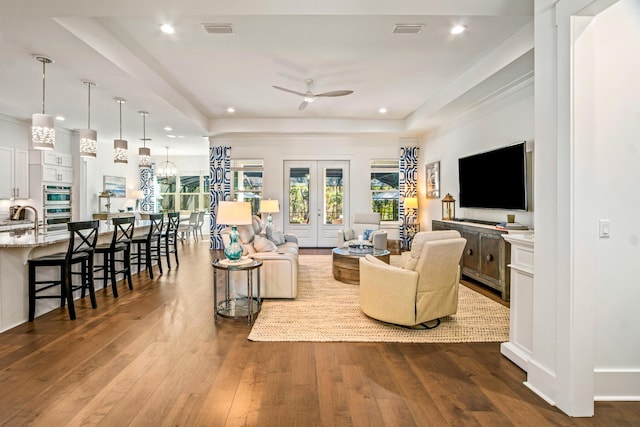 living room with ceiling fan with notable chandelier, wood-type flooring, sink, a tray ceiling, and french doors