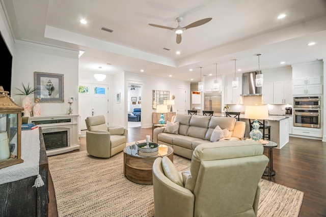 living room with hardwood / wood-style flooring, ceiling fan, and a raised ceiling