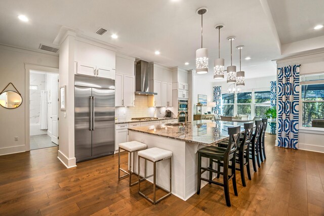 kitchen featuring wall chimney range hood, stainless steel appliances, white cabinets, and a center island with sink