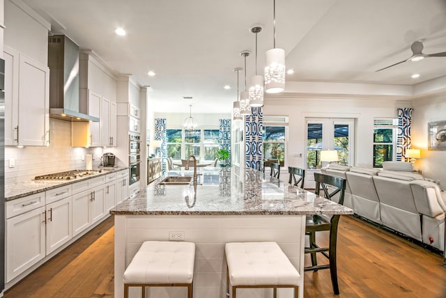 kitchen with pendant lighting, white cabinetry, sink, a kitchen breakfast bar, and wall chimney range hood