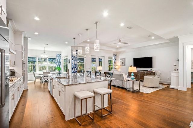 kitchen featuring stone countertops, a kitchen island with sink, hanging light fixtures, white cabinets, and a kitchen bar