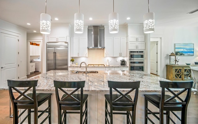 kitchen featuring a kitchen bar, appliances with stainless steel finishes, pendant lighting, wall chimney range hood, and white cabinets