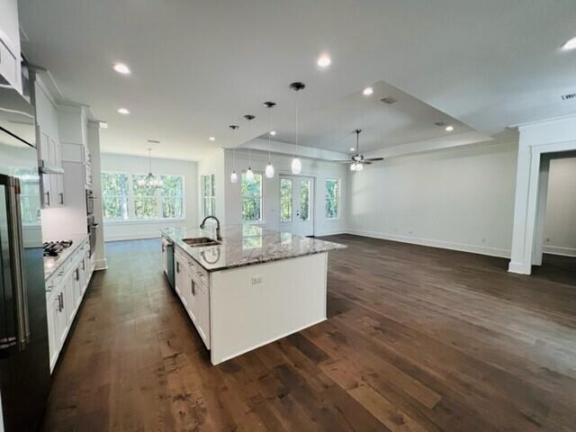 kitchen featuring pendant lighting, sink, white cabinets, light stone counters, and a center island with sink