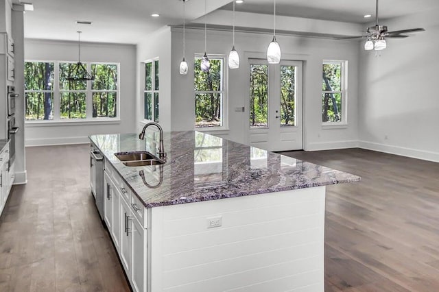 kitchen with sink, dark wood-type flooring, dark stone countertops, hanging light fixtures, and white cabinets