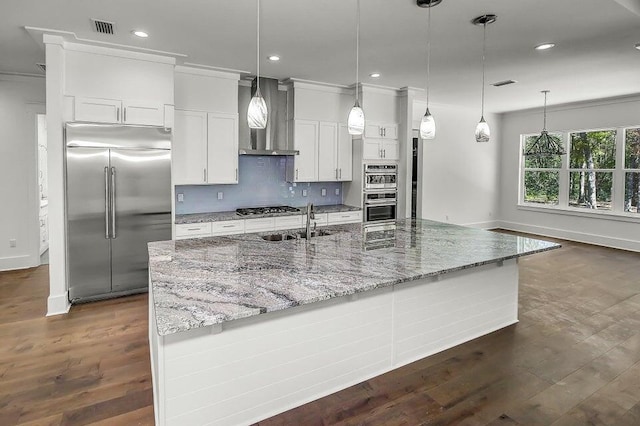 kitchen with wall chimney range hood, hanging light fixtures, stainless steel appliances, light stone counters, and white cabinets