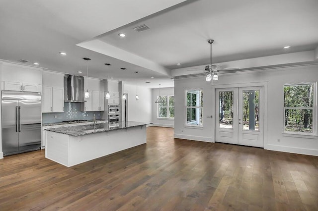 kitchen with appliances with stainless steel finishes, decorative light fixtures, dark stone countertops, white cabinets, and a kitchen island with sink