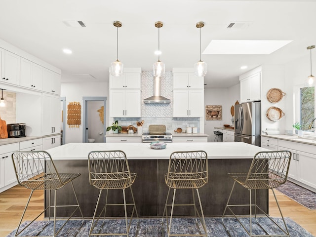 kitchen with a large island, appliances with stainless steel finishes, a kitchen bar, and wall chimney range hood