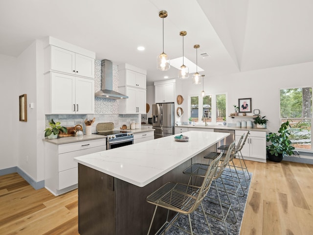 kitchen featuring stainless steel appliances, a center island, wall chimney range hood, and white cabinets