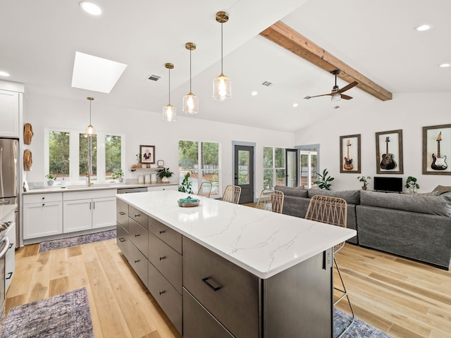 kitchen featuring a breakfast bar area, hanging light fixtures, a wealth of natural light, light stone countertops, and white cabinets