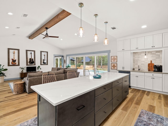 kitchen featuring hanging light fixtures, vaulted ceiling with beams, light stone counters, light hardwood / wood-style floors, and white cabinets