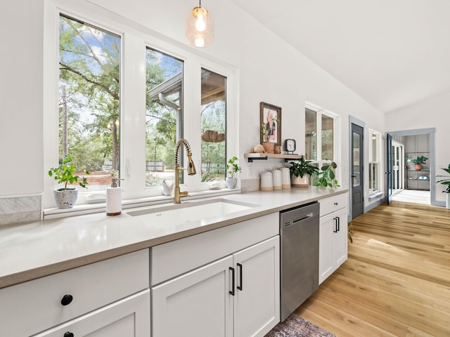 kitchen with sink, light hardwood / wood-style flooring, white cabinets, vaulted ceiling, and stainless steel dishwasher