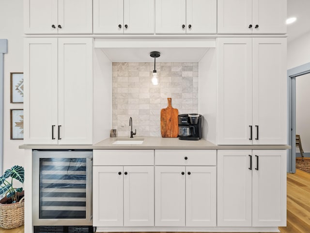 bar with sink, hanging light fixtures, wine cooler, tasteful backsplash, and light wood-type flooring