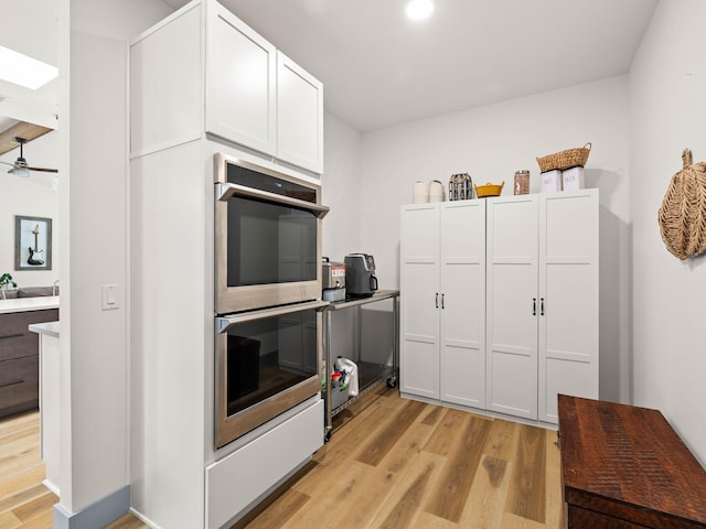 kitchen featuring light wood-type flooring, ceiling fan, double oven, and white cabinets