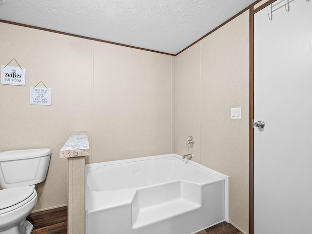 bathroom with toilet, wood-type flooring, a textured ceiling, ornamental molding, and a bathing tub