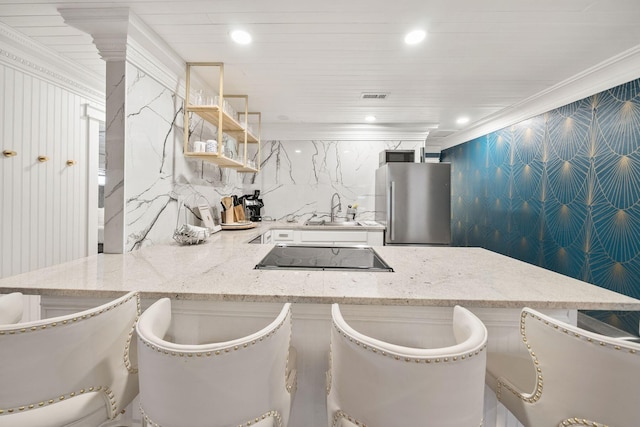 kitchen featuring light stone counters, ornamental molding, black electric stovetop, and stainless steel fridge