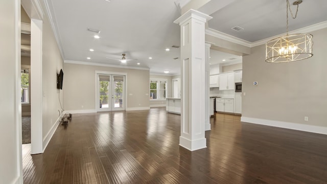 unfurnished living room featuring dark wood-type flooring, french doors, decorative columns, crown molding, and ceiling fan with notable chandelier