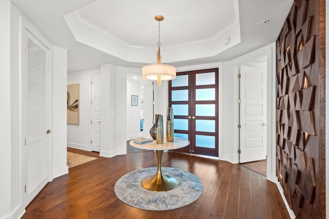 entryway with dark wood-type flooring, ornamental molding, and a raised ceiling