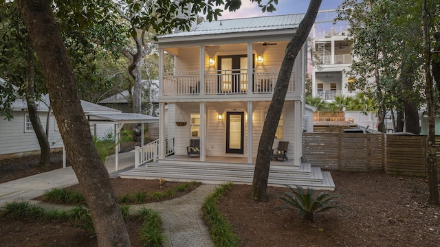 back house at dusk featuring a porch and a balcony