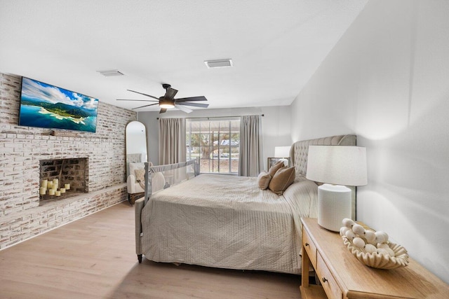 bedroom featuring a brick fireplace, wood-type flooring, and ceiling fan