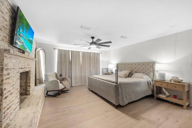 bedroom with a fireplace, ceiling fan, and light hardwood / wood-style flooring