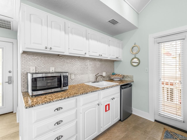 kitchen with white cabinetry, dark stone counters, dishwashing machine, and sink