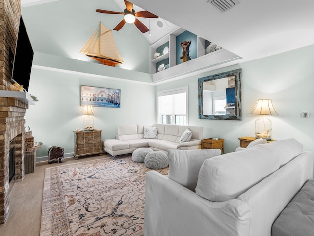 living room with a brick fireplace, high vaulted ceiling, and ceiling fan