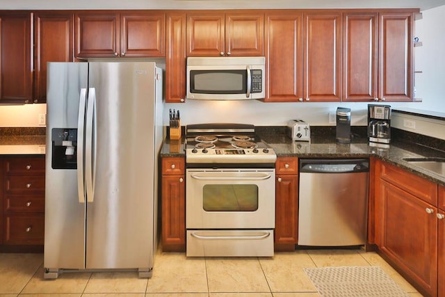 kitchen with light tile patterned floors, dark stone counters, and appliances with stainless steel finishes