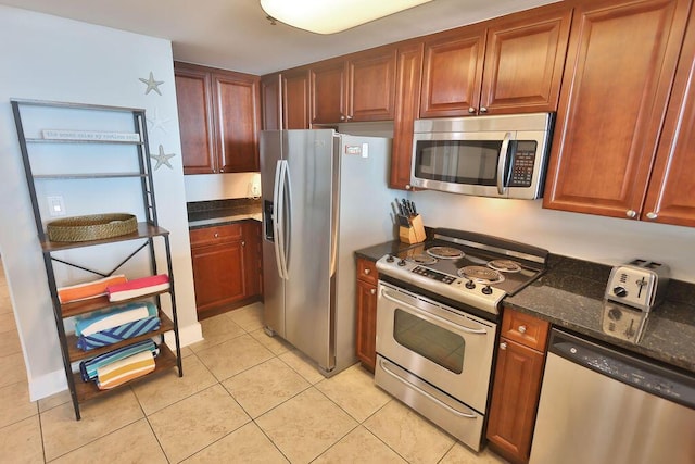 kitchen featuring light tile patterned flooring, appliances with stainless steel finishes, and dark stone counters