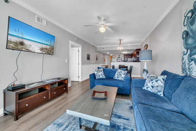 1110 Santa Rosa Blvd Unit C601, Fort Walton Beach, FL 32548 - living room featuring a wainscoted wall, visible vents, light wood-style flooring, ornamental molding, and ceiling fan with notable chandelier