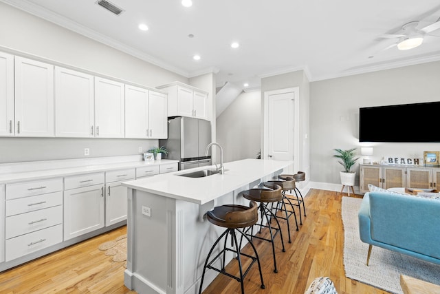 kitchen featuring stainless steel refrigerator, white cabinetry, sink, a breakfast bar area, and a center island with sink