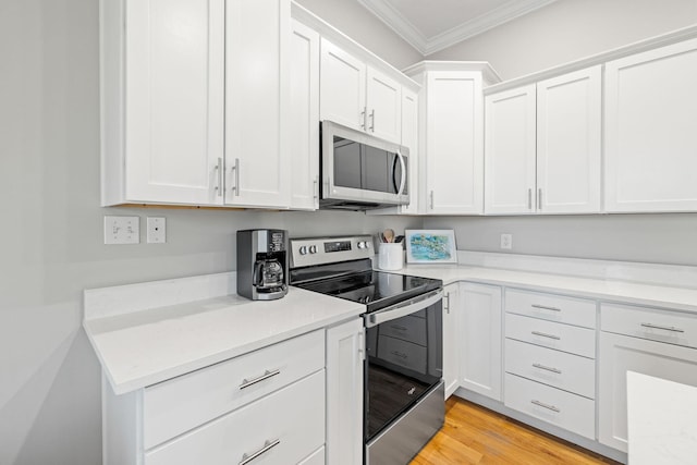 kitchen with ornamental molding, appliances with stainless steel finishes, light wood-type flooring, and white cabinets