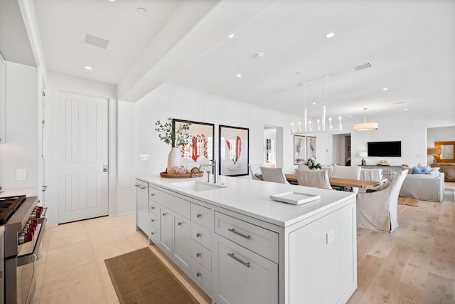 kitchen featuring sink, hanging light fixtures, a kitchen island with sink, stainless steel range, and light wood-type flooring