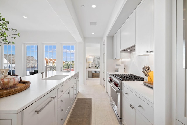 kitchen featuring white cabinetry, wall chimney range hood, stainless steel stove, and sink