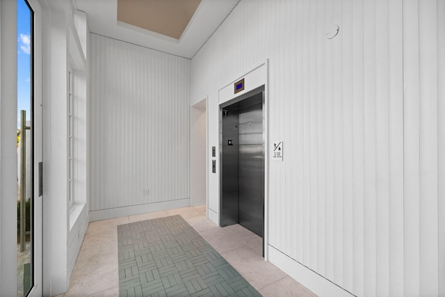 corridor featuring elevator, a tray ceiling, and light tile patterned floors