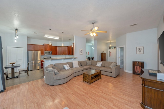 living room featuring ceiling fan, a textured ceiling, and light hardwood / wood-style floors