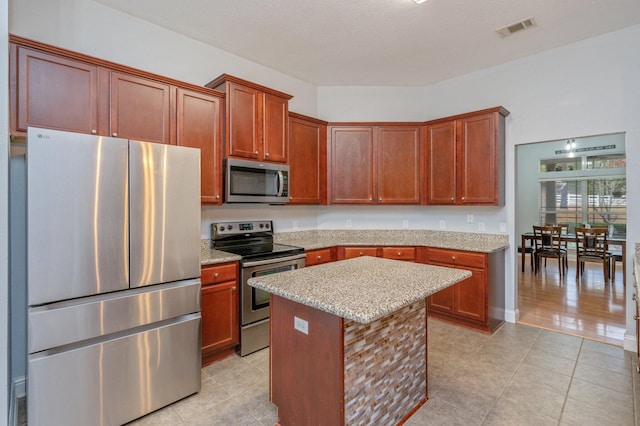 kitchen with light stone counters, stainless steel appliances, a center island, and light tile patterned flooring