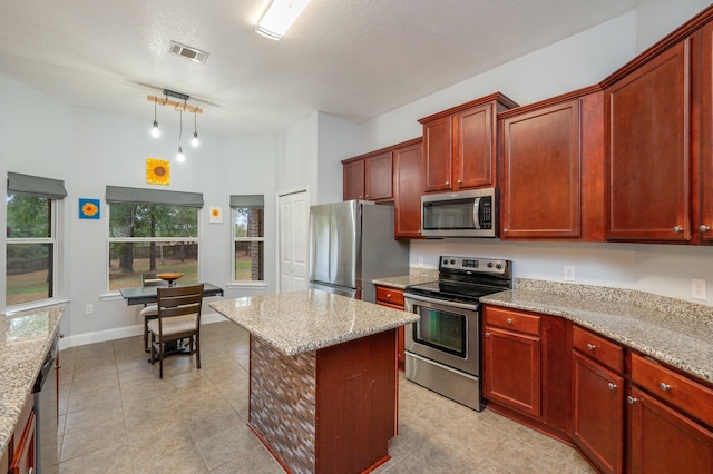 kitchen with appliances with stainless steel finishes, a kitchen island, light stone countertops, and hanging light fixtures