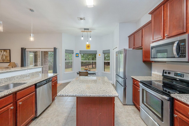 kitchen featuring light tile patterned flooring, a kitchen island, appliances with stainless steel finishes, pendant lighting, and light stone countertops