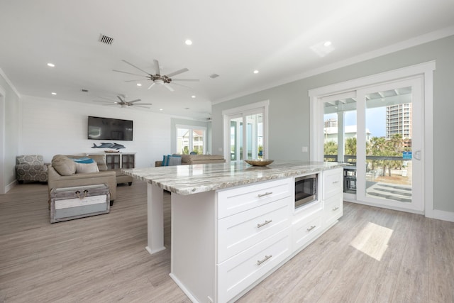 kitchen featuring white cabinetry, stainless steel microwave, a kitchen island, a healthy amount of sunlight, and light stone countertops