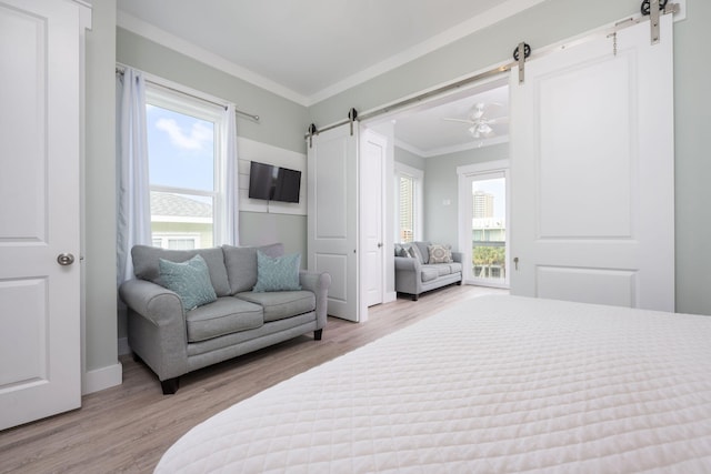 bedroom featuring ornamental molding, a barn door, multiple windows, and light wood-type flooring