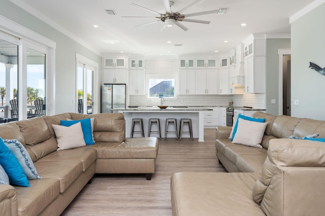 living room with ornamental molding, light hardwood / wood-style floors, and ceiling fan