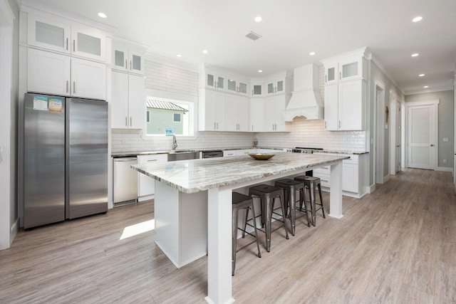 kitchen with stainless steel appliances, a center island, light stone counters, custom range hood, and white cabinets