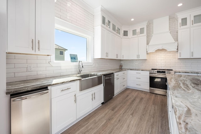 kitchen featuring stainless steel appliances, light stone countertops, custom range hood, and white cabinets