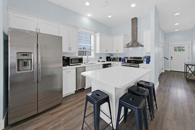 kitchen featuring appliances with stainless steel finishes, white cabinets, a kitchen breakfast bar, and wall chimney exhaust hood