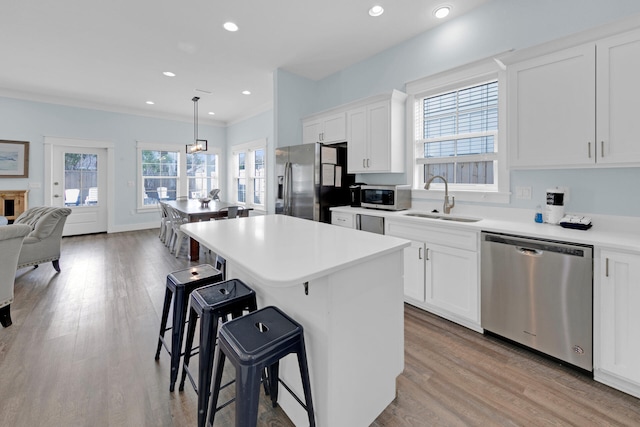 kitchen with sink, appliances with stainless steel finishes, white cabinetry, a center island, and decorative light fixtures