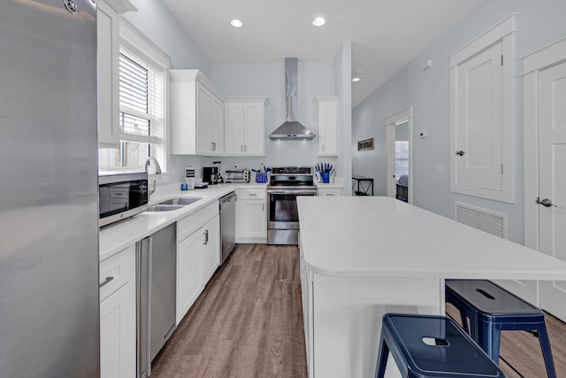 kitchen with wall chimney range hood, a kitchen breakfast bar, stainless steel appliances, and a center island