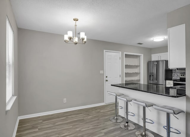 kitchen with decorative light fixtures, stainless steel fridge, a kitchen breakfast bar, kitchen peninsula, and white cabinets