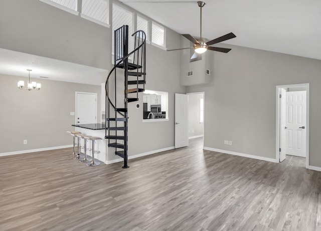 unfurnished living room with hardwood / wood-style flooring, ceiling fan with notable chandelier, and high vaulted ceiling